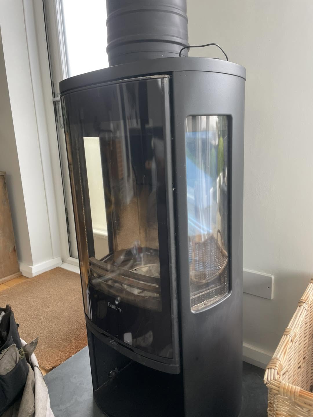 Tall black stove with clear glass, back in its corner after the restoration