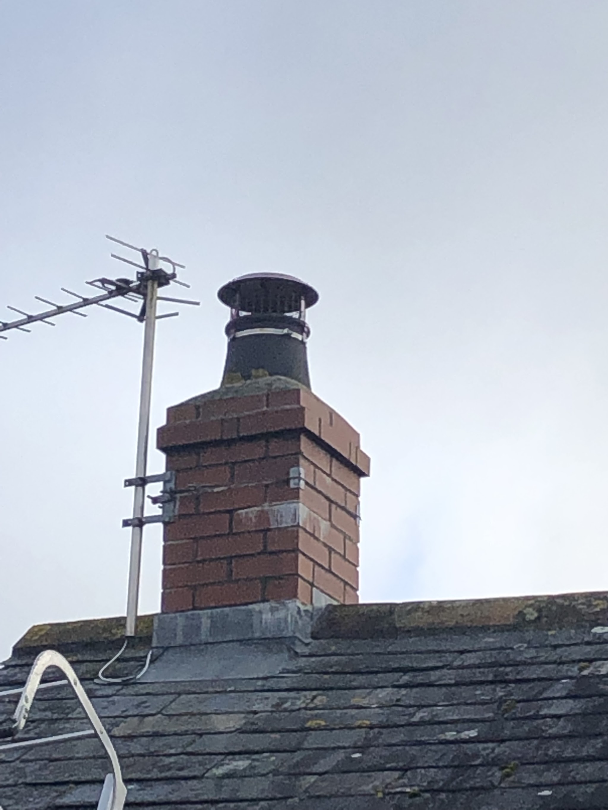 Brick chimney stack with a cowl fitted, on a slate roof